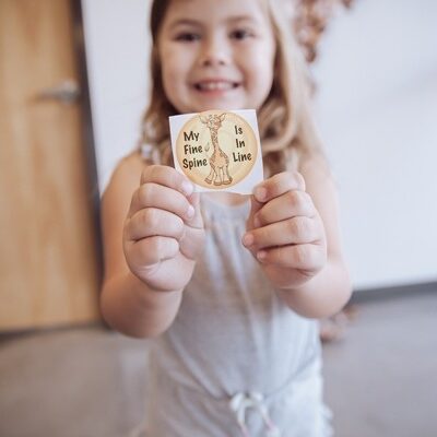 Child holding a sticker that says "My fine spine is in line"